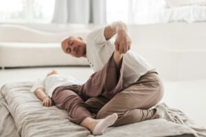 Person performing gentle back stretches on a mat beside a chair in a bright home room.